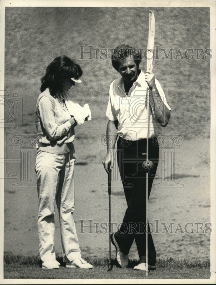 1984 Press Photo Golfer Rex Caldwell holds flag as wife Janet cleans golf ball- Historic Images