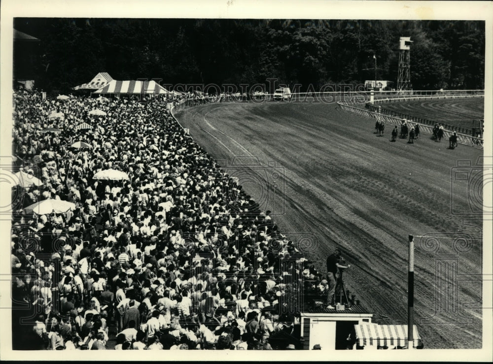 1987 Press Photo Large crowd lines the fence as horses come around the turn- Historic Images