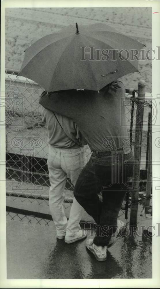 1990 Press Photo Two people huddle under umbrella at Saraotga Race Track, NY- Historic Images