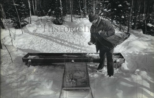 1984 Press Photo Robert B. Sabbann spreading food into a deer feeder in Brule - Historic Images