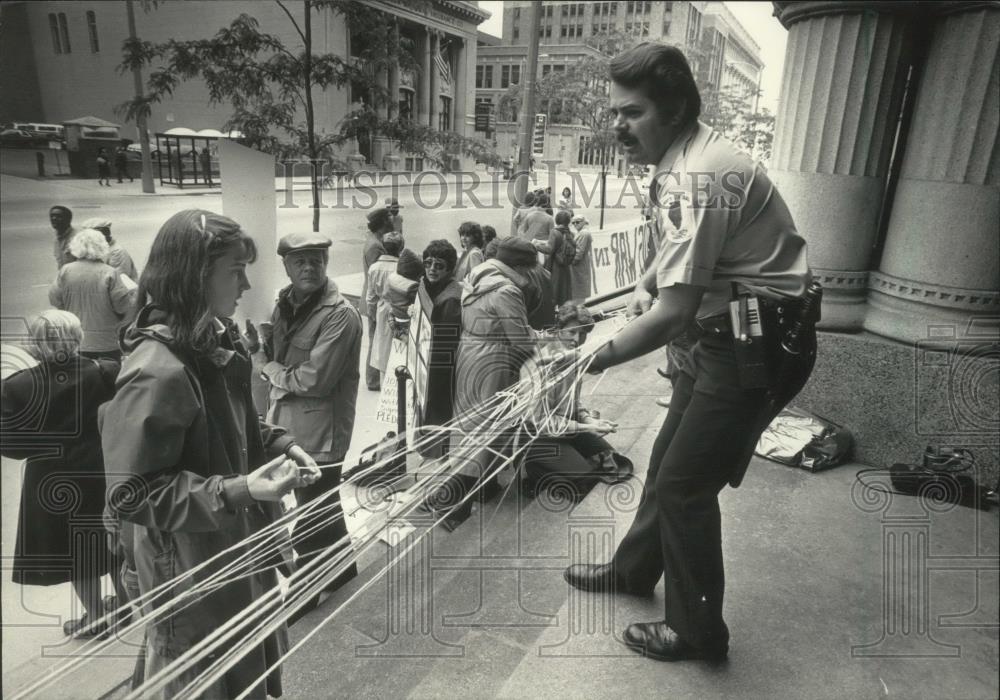 1985 Press Photo Security guard removes string during protest. Milwaukee - Historic Images