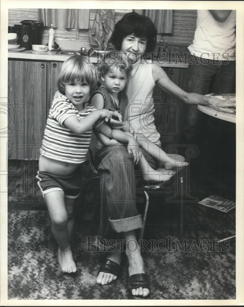 Press Photo Woman sitting in Chair with Two Children playing around her - Historic Images