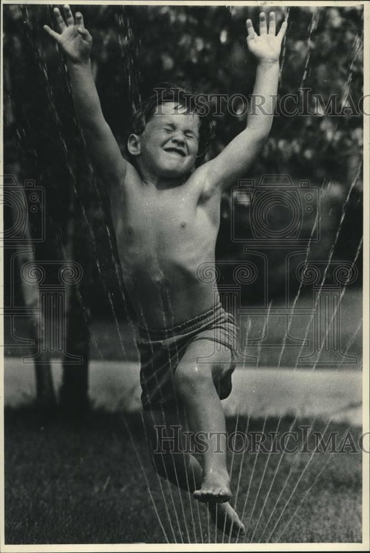 1983 Press Photo Jonathan Arndt cools summer heat off using a sprinkler - Historic Images