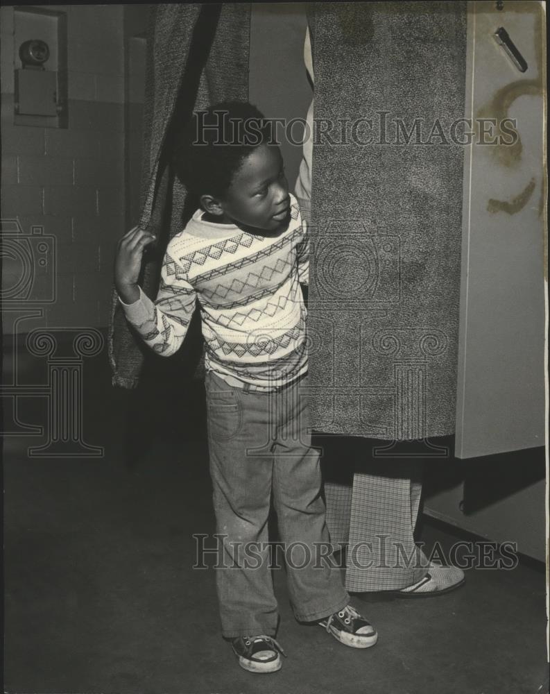 1977 Press Photo Young boy looking out of curtain from voting booth - abna26531 - Historic Images