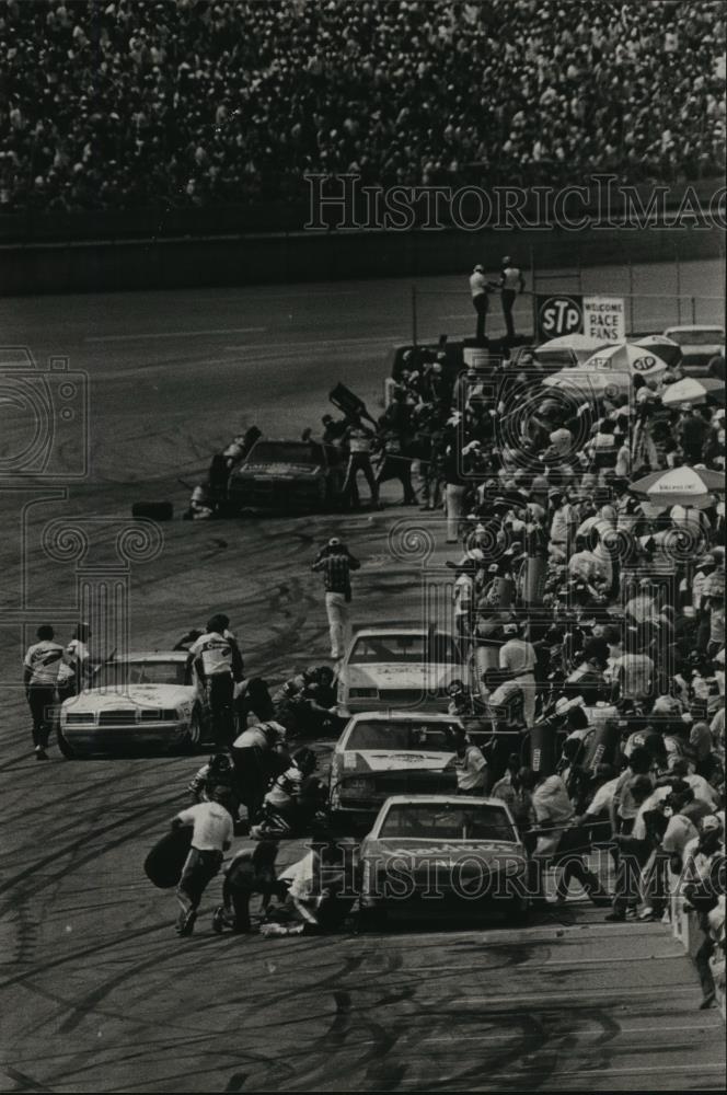 1984 Press Photo Cars take pit stops while caution flags fly at race, Alabama - Historic Images