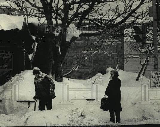 1979 Press Photo Woman waits for bus as man shovels walk Wisconsin - mjc18091 - Historic Images