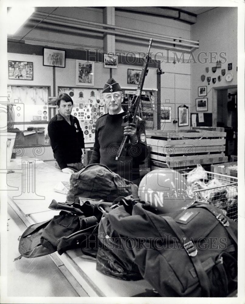 Press Photo Man holds up rifle among military items - Historic Images