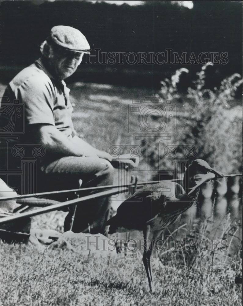 Press Photo Fisherman Feeds Heron On Riverbank Of Amsterdam - Historic Images