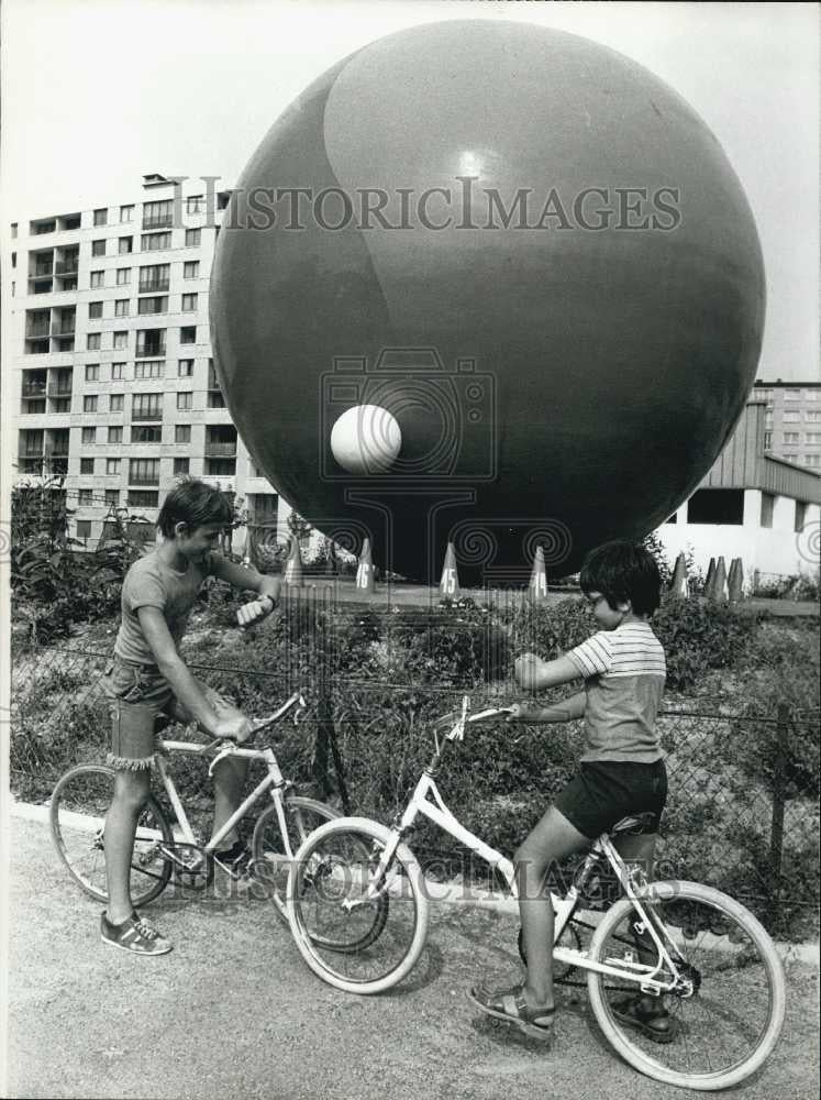 1976 Press Photo Two Boys on Bike Compare Watches Under Large Red Ball Clock - Historic Images