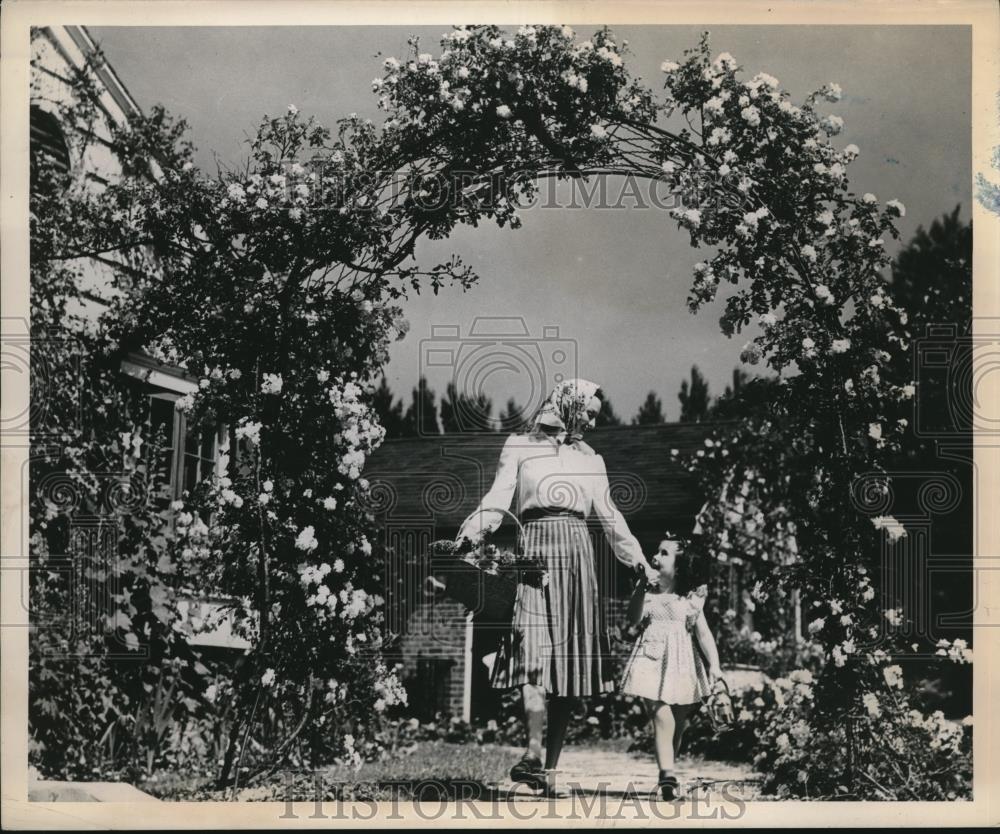 1949 Press Photo Lady With Child Walking Under Large Trellis of Climbing Roses - Historic Images