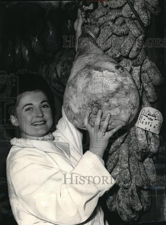 1966 Press Photo Lady says "cheese" while holding ham hanging amid sausages - Historic Images