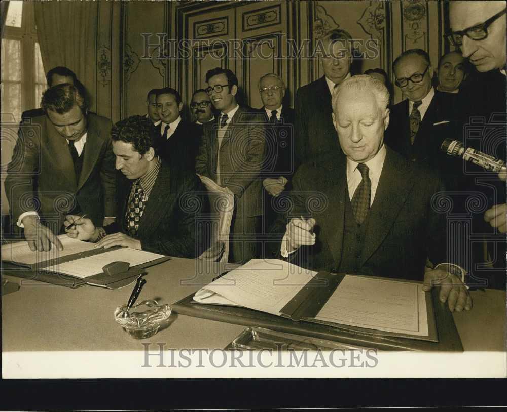 Press Photo Two Men Signing Documents While Others Watch - Historic Images