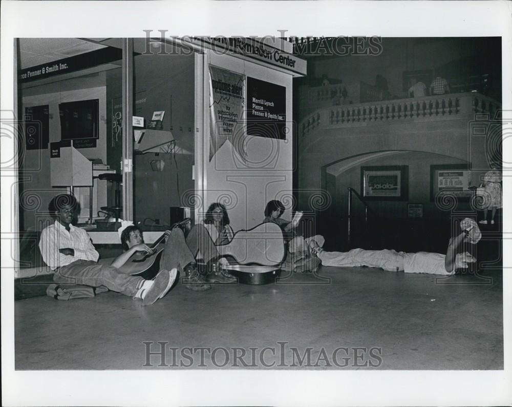 Press Photo Musicians Rest On The Floor Near An Information Center - Historic Images