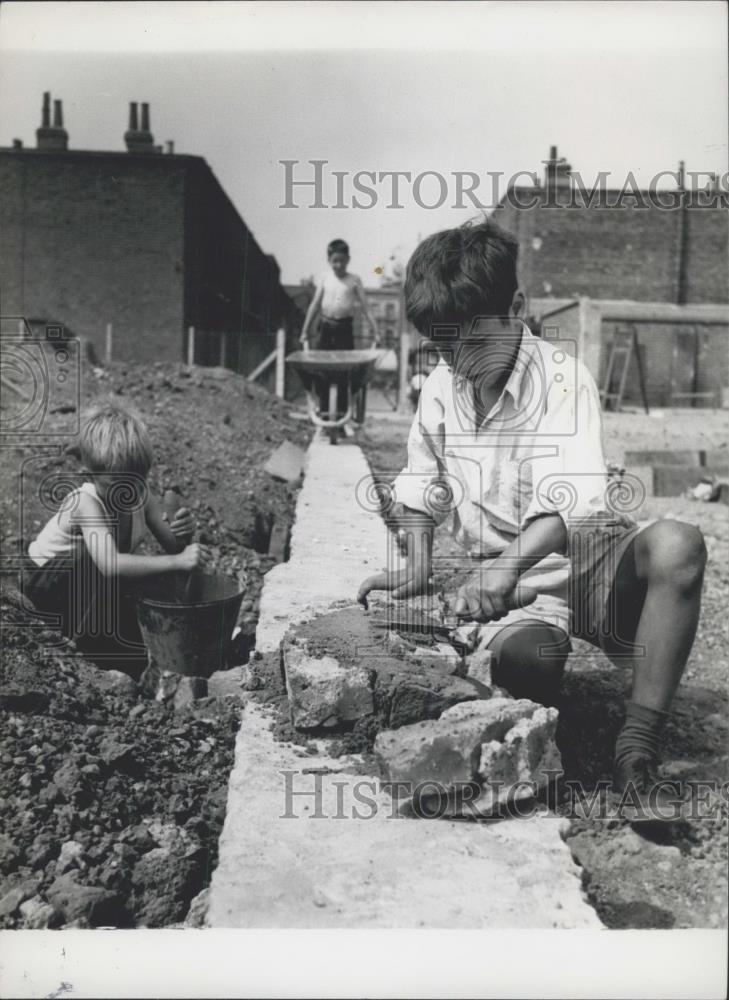 Press Photo Brain Gardner laying the bricks while 2 friend help - Historic Images