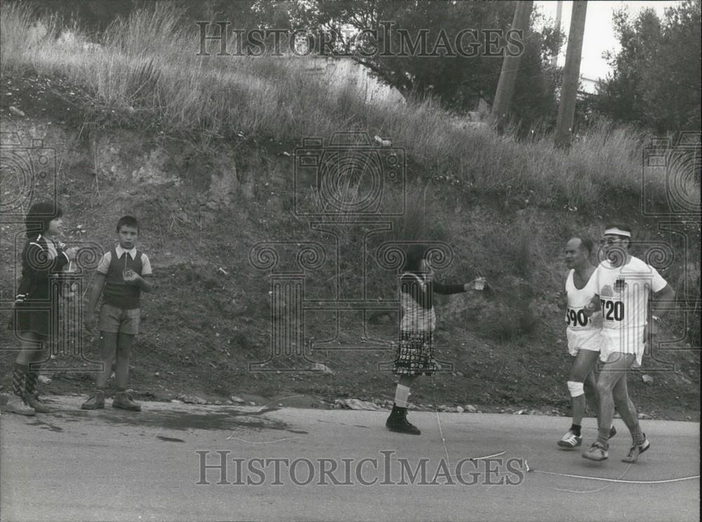 Press Photo Girl Holding Out Water To Two Runners In Race - Historic Images
