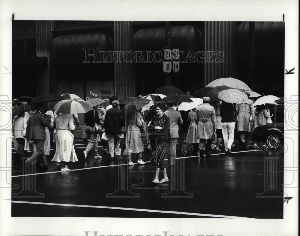 1986 Press Photo Pedestrian walks against the tide of umbrella crossing square - Historic Images