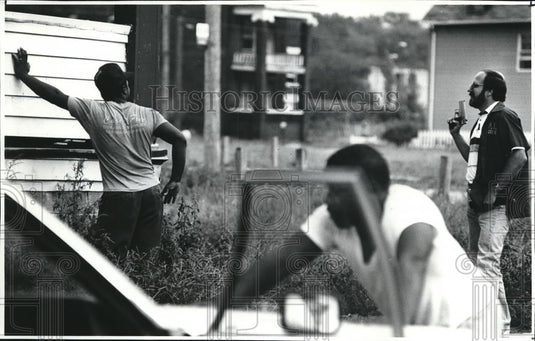 1991 Press Photo An officer with a gun after finding suspected men outside - Historic Images