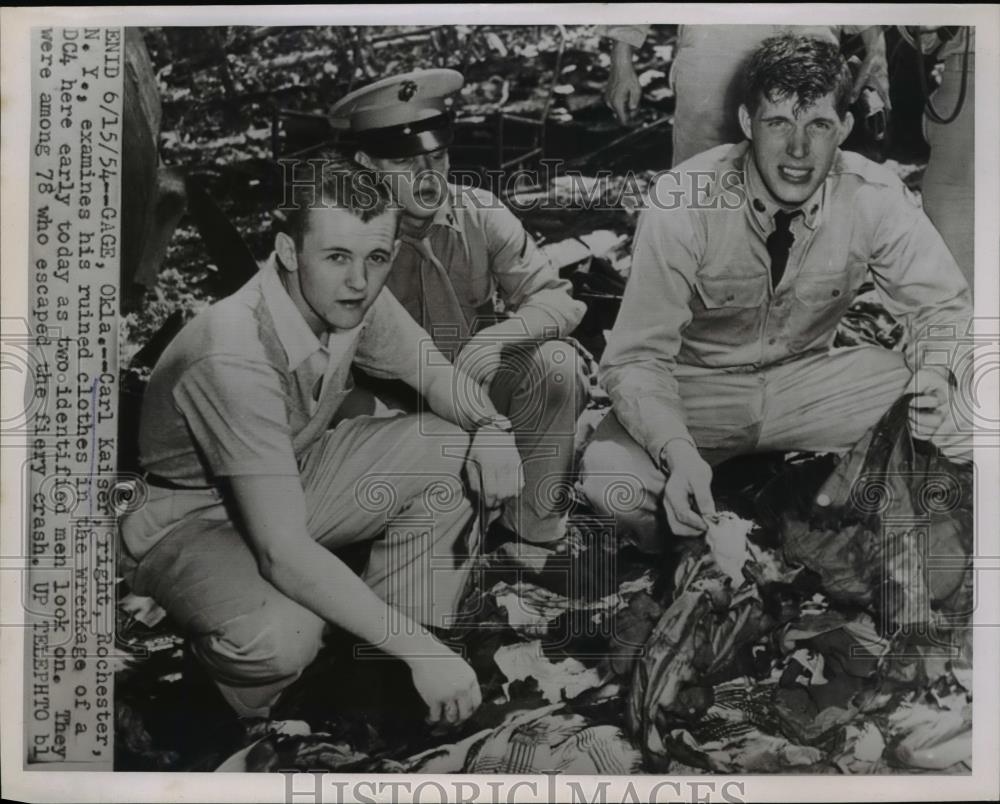 1954 Press Photo Carl Kaiser, Examines ruined clothes in wreckage of Dc4 - Historic Images