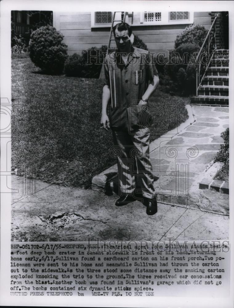 1956 Press Photo John Sullivan stands in deep bomb crater in from of his home - Historic Images