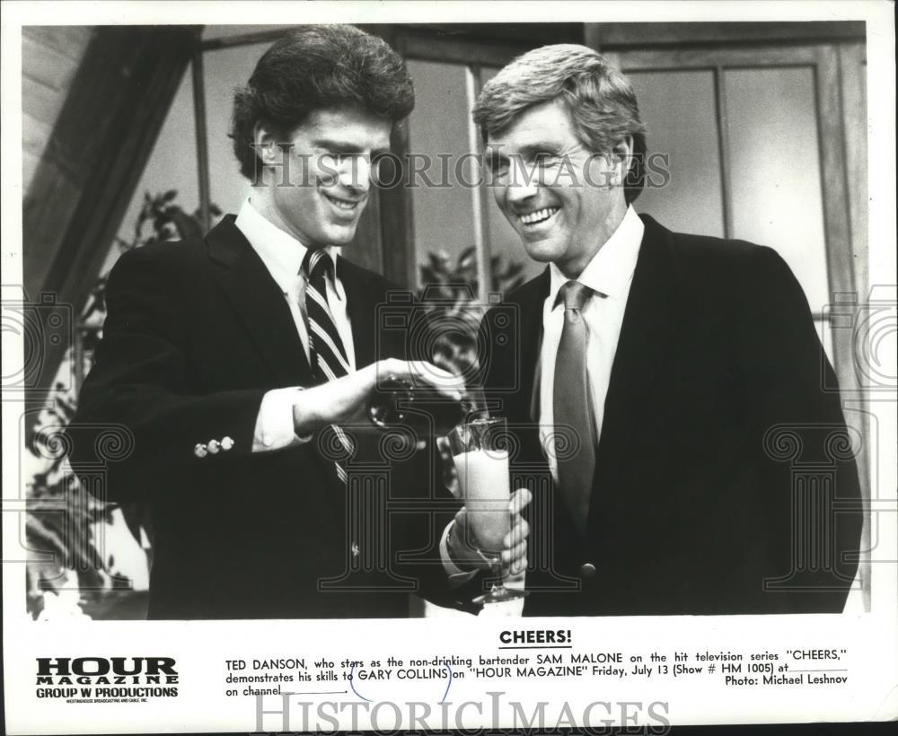 1985 Press Photo Ted Danson demonstrates his bartending skills to Gary Collins - Historic Images