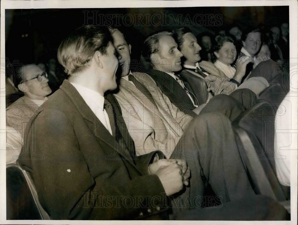 Press Photo Tall men try to sit in seats for shorter people - Historic Images