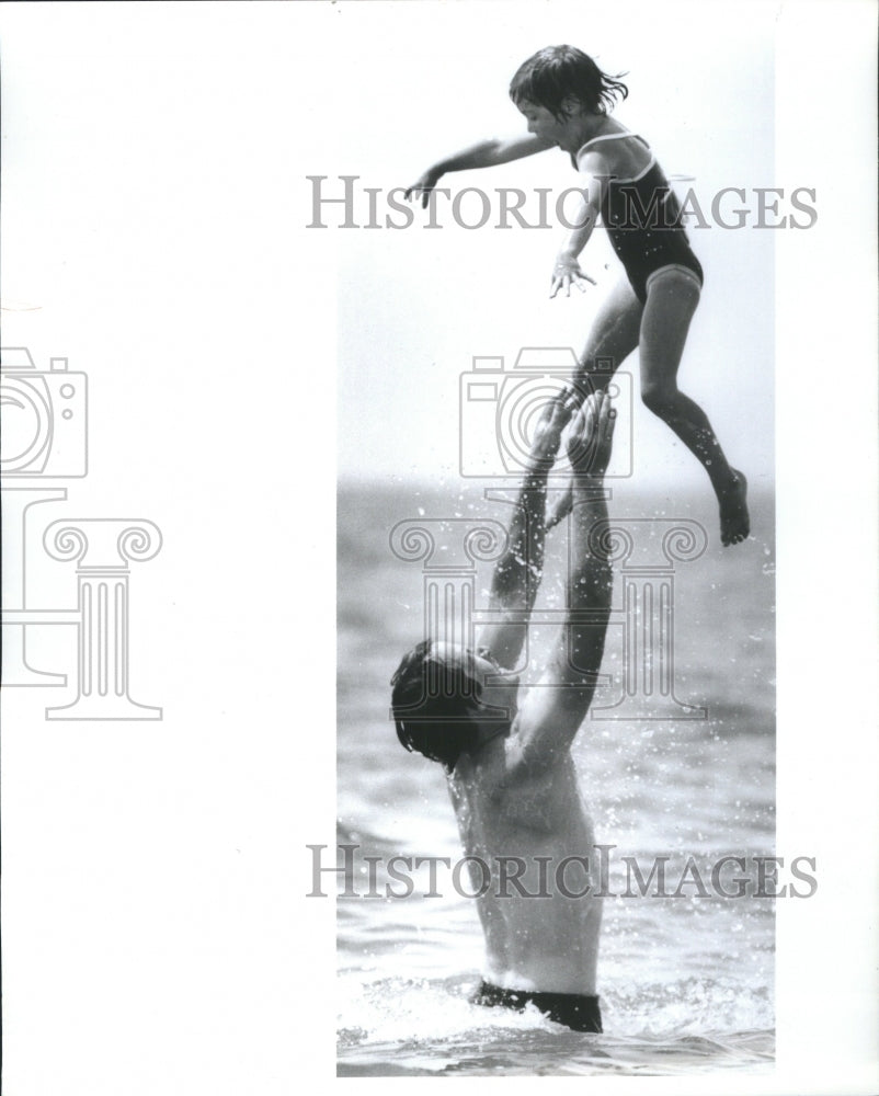 1985 Press Photo Mark Susin throws daugther up at beach