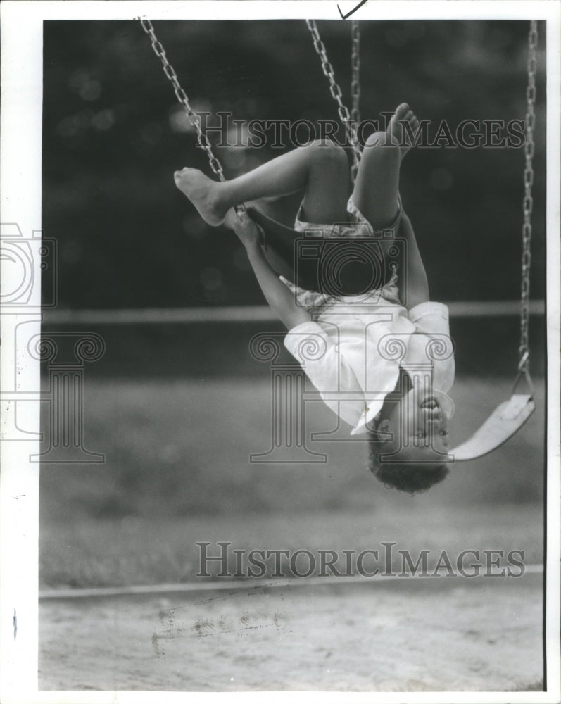 1987 Press Photo Child Hanging Upside Down In Swing