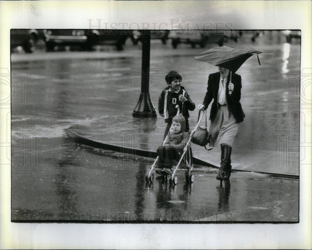 women carrying son rainy day umbrella - Historic Images