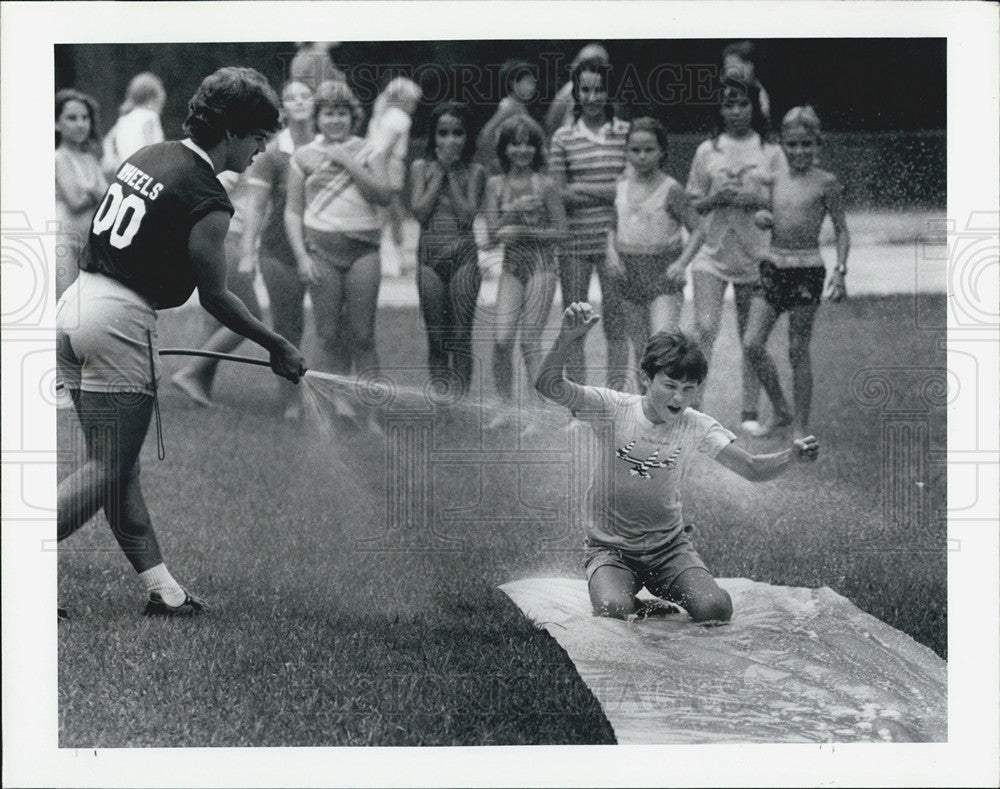 1984 Press Photo Coach Larry Feenur allows Eric Snell down the Slip + Slide - Historic Images