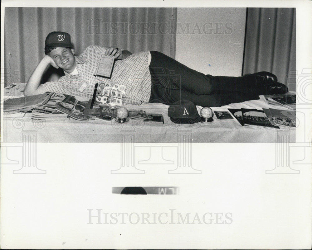 Press Photo Sports fan lays on table covered in baseball memorabilia - Historic Images