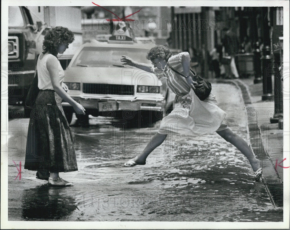 1988 Press Photo Woman leaps over rushing water due to water main break Boston - Historic Images