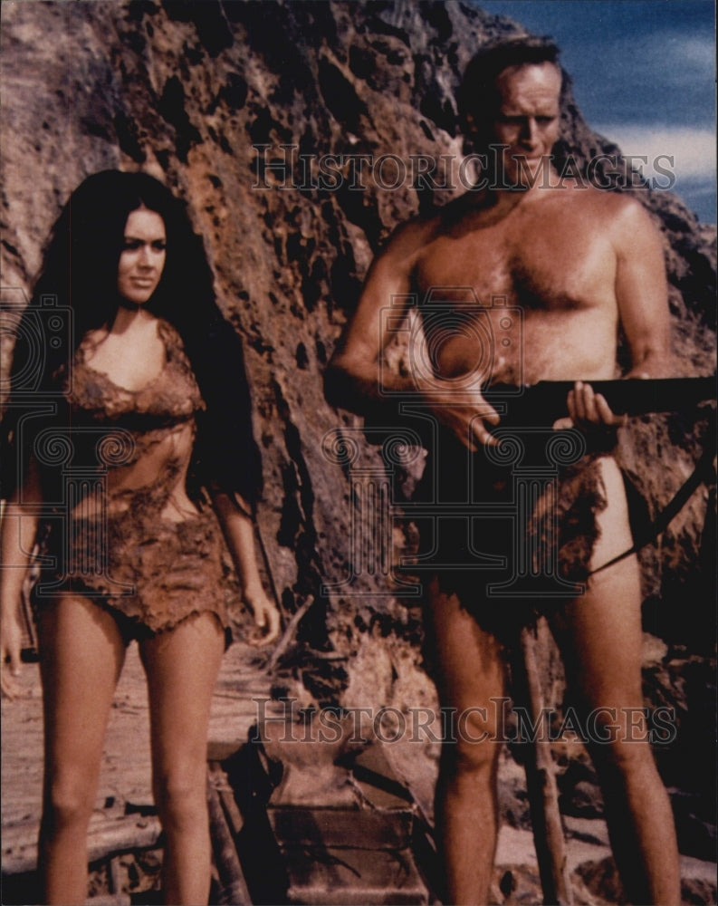 Press Photo Actor in a loin cloth holding machine gun with brunette actress - Historic Images