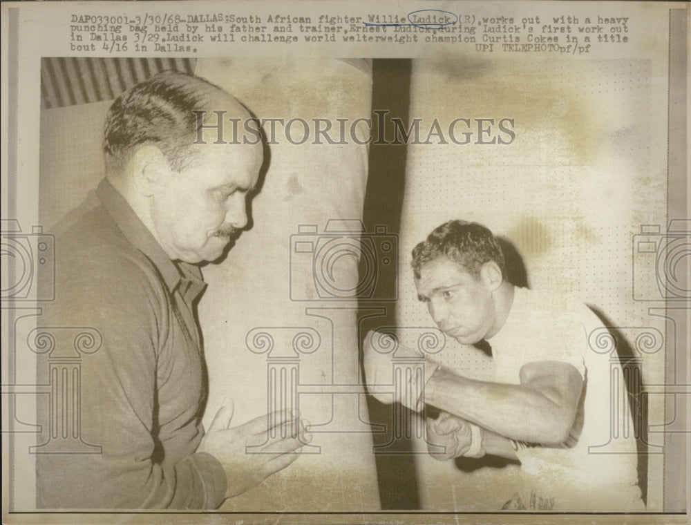 1968 Willie Ludick hits heavy punching bag while his father holds it - Historic Images