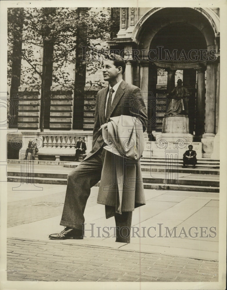 Undated Ralph Lowe holding a coat and standing in front of stone statue - Historic Images