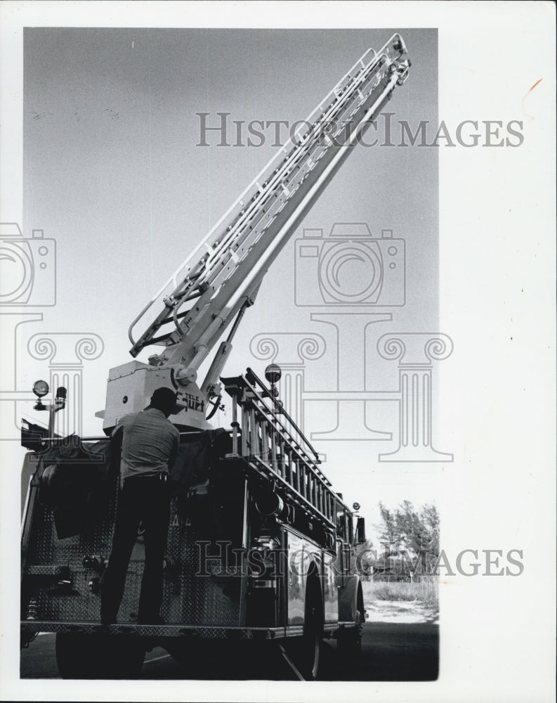 1977 Fireman raising ladder on truck. - Historic Images