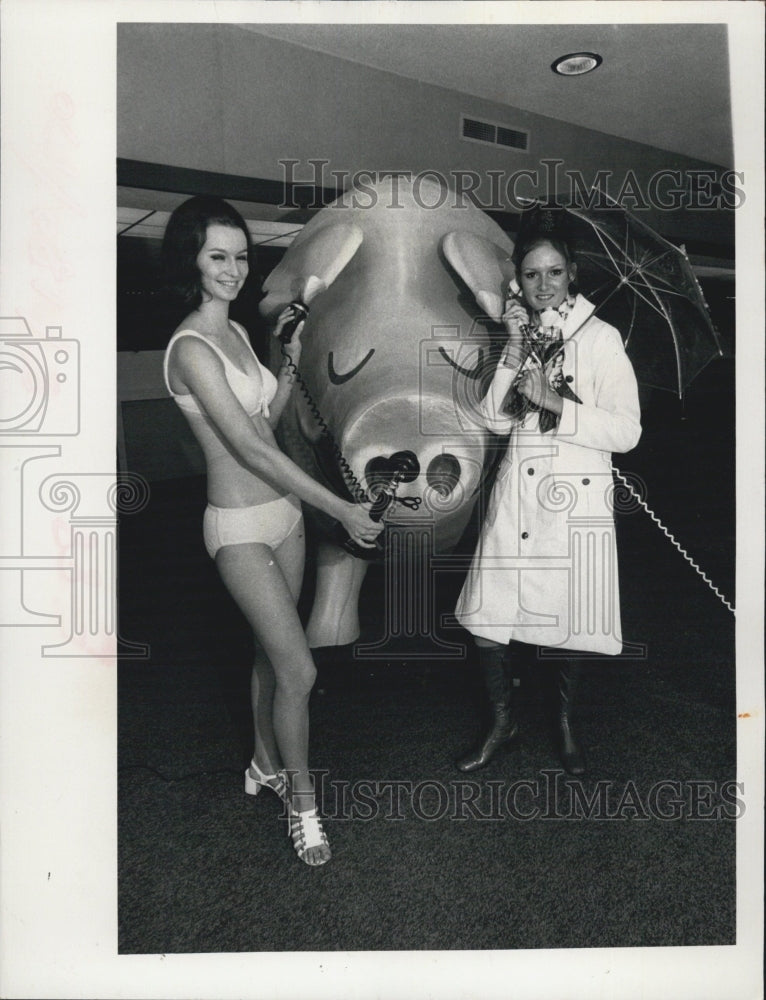 1972 Girls in Bathing Suit and raincoat holding a phone. - Historic Images