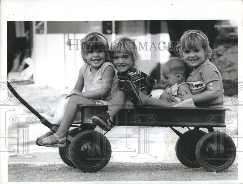 1984 Young children getting pulled in wagon by Mom.  - Historic Images