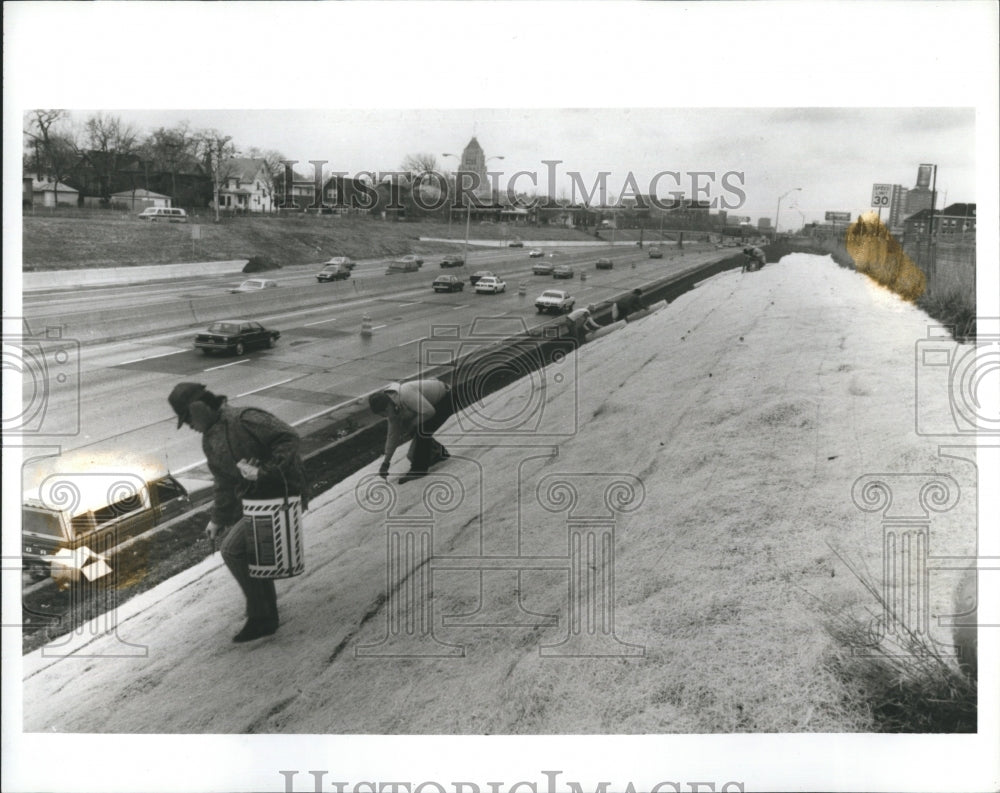 1986 Workers cover grass seeds with wood blanket by freeway - Historic Images