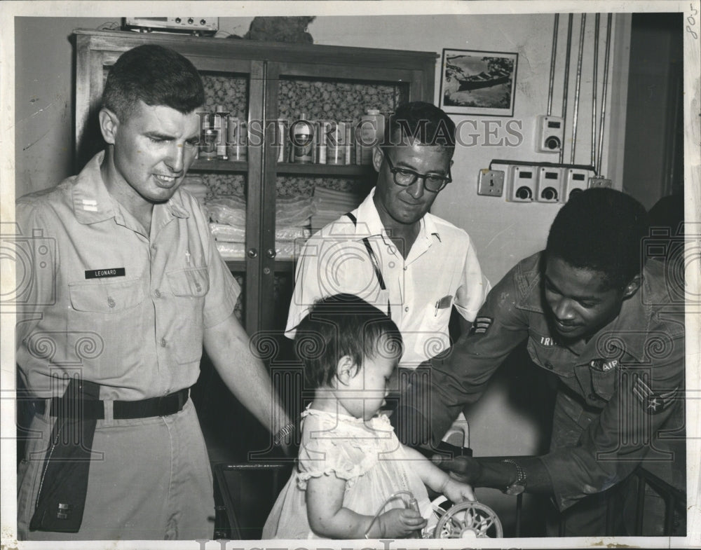 1967 Press Photo Air Force men aid teaches orphan to play a pinwheel. - Historic Images