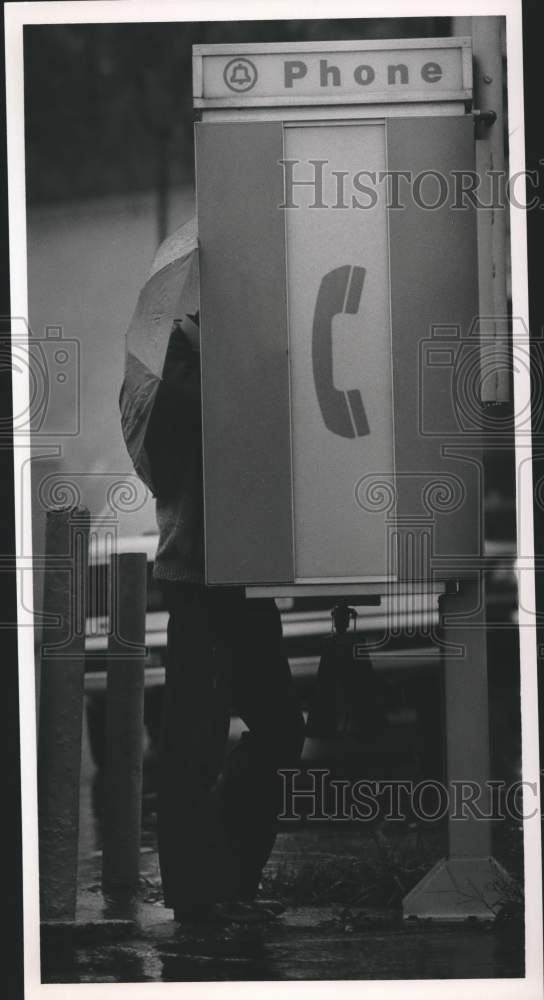 1986 Press Photo Umbrella-covered Pedestrian Uses Outside Pay Phone in Hoover - Historic Images