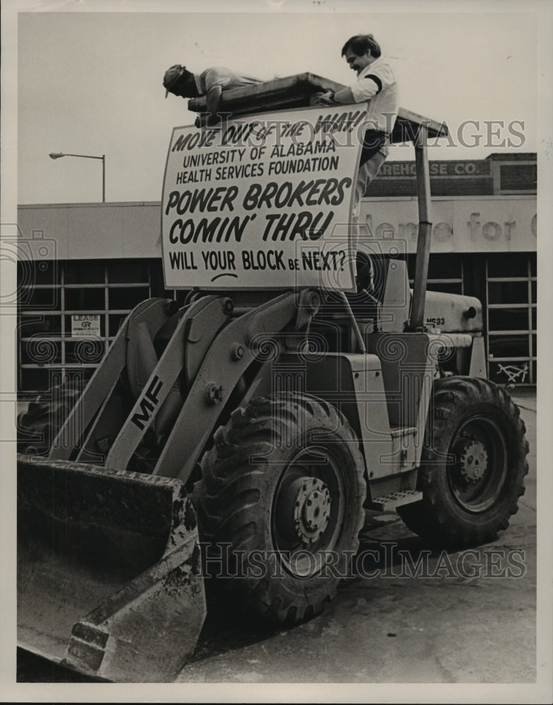 1987, David Baily and George Sarris place clinic sign on bulldozer - Historic Images