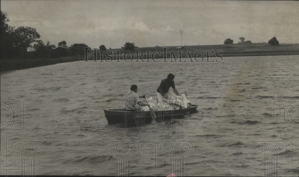 1975 James Bond and prisoner feed fish by boat at Greensboro Lake - Historic Images