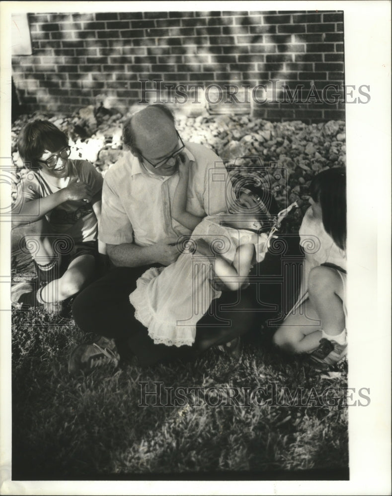 1982, Sara Hodgin sits in her father&#39;s lap in yard - abna31731 - Historic Images