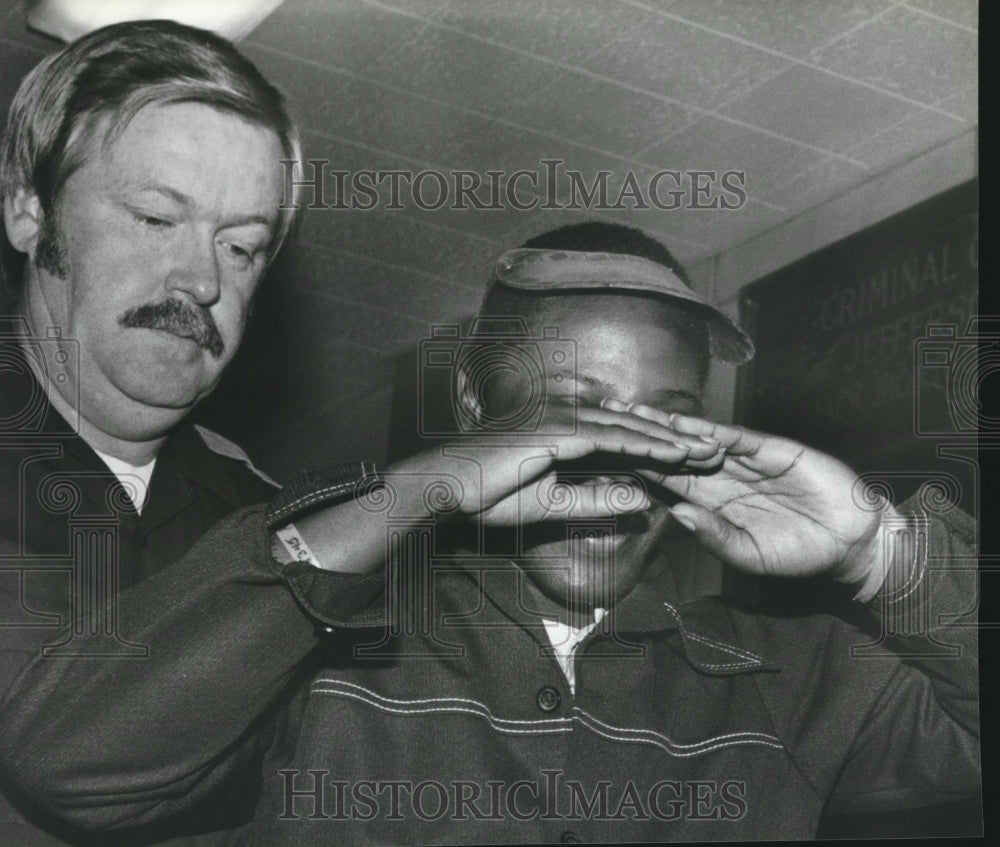 1980, Tommy Lee Hines shields eyes as he enters court with Officer - Historic Images