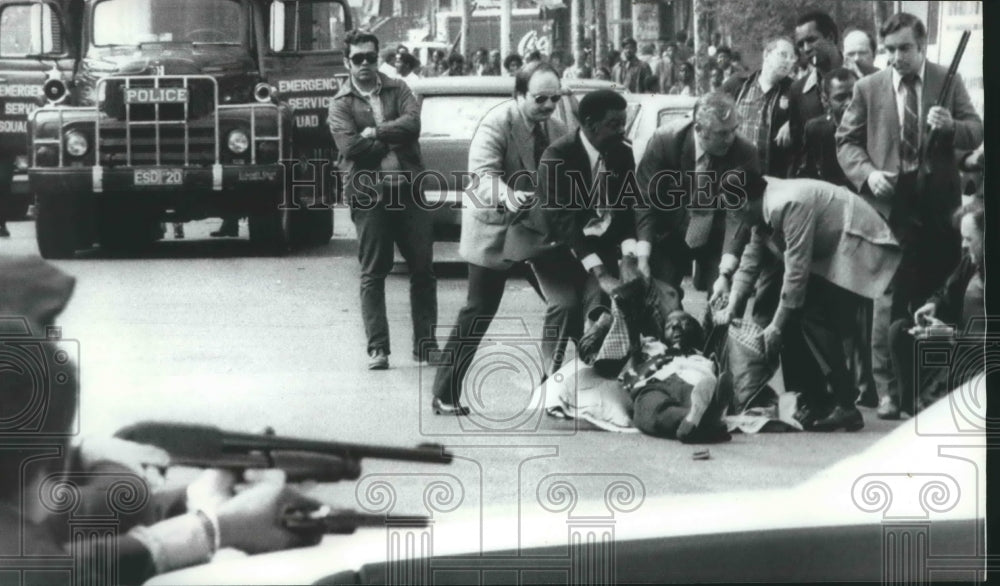 1972, Mace Brown on street being assisted by unidentified others - Historic Images