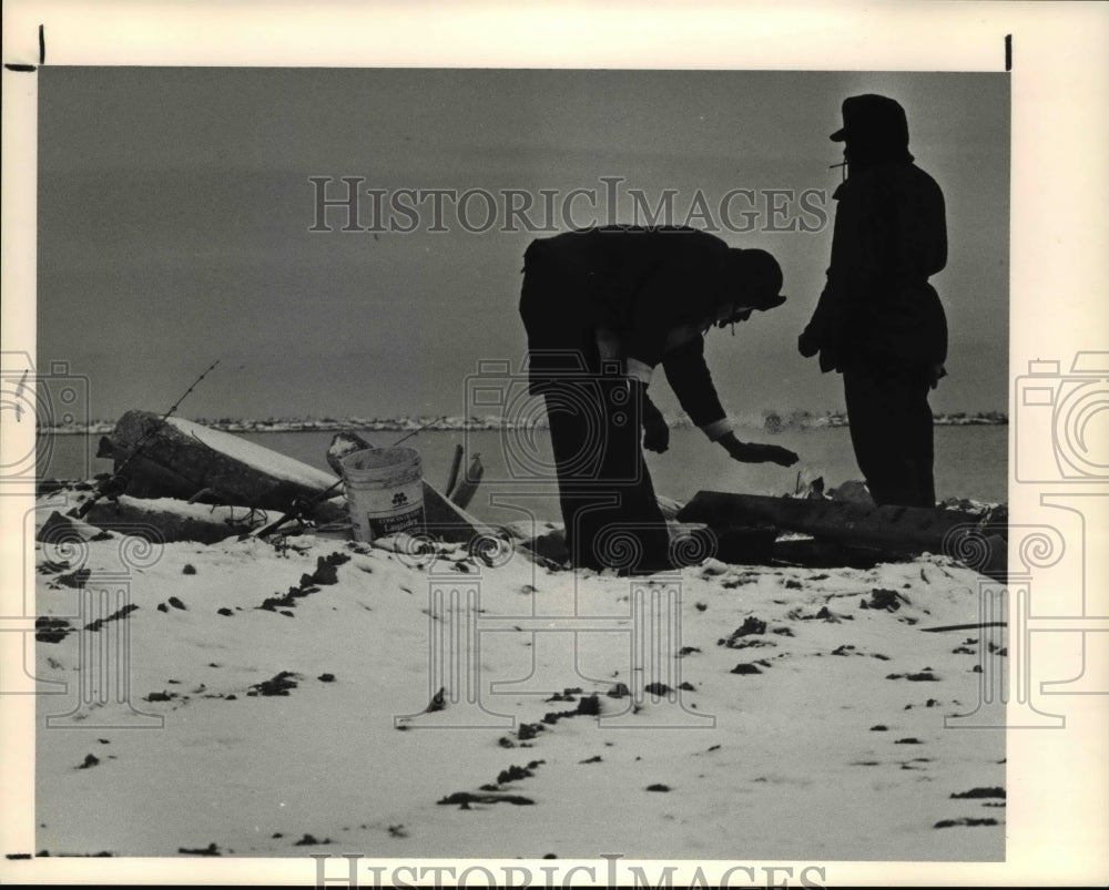 1990 Press Photo Nate Savage warms his hands over a small fire while fishing - Historic Images