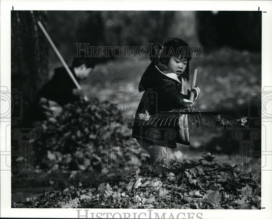 1990 Press Photo Shoko Nakamura, 4, rakes leaves with her brother Hiroko, 9, - Historic Images