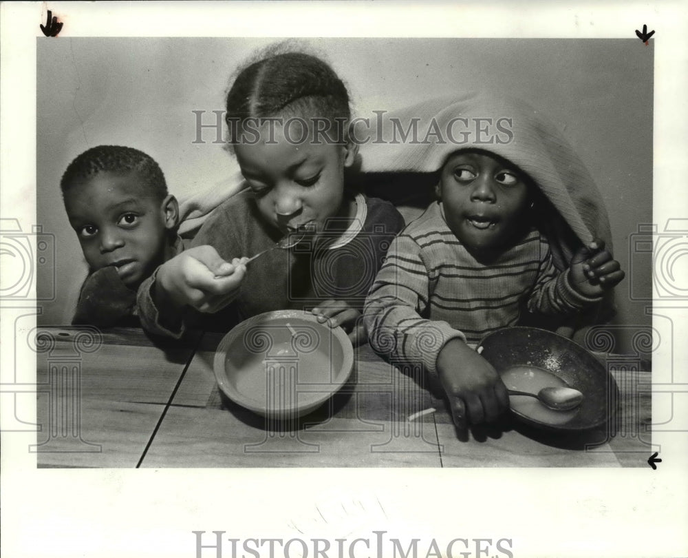 1982 Press Photo Three children eat warm chicken noodle soup while wrapped up - Historic Images