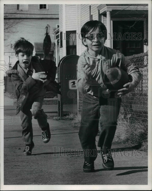 1974, Mario Simons and Danny Adams run down the sidewalk holding ball - Historic Images