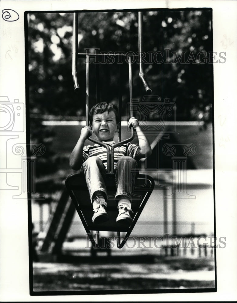 1985 Press Photo Gregory Koeka Tries Out One of the Swings at the Lakewood Park - Historic Images